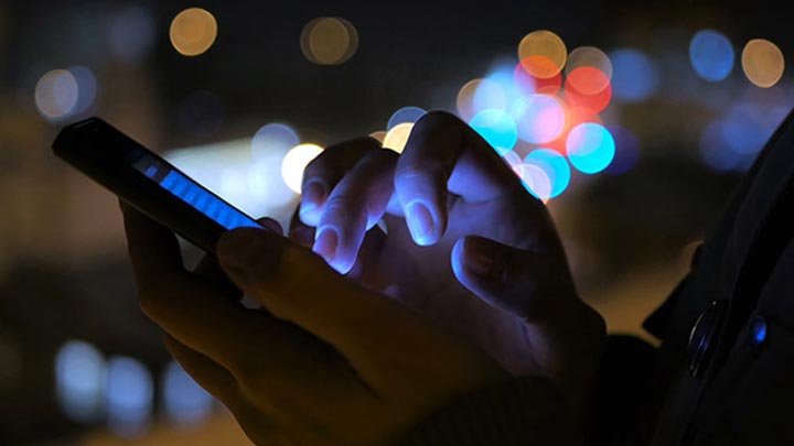 Pair of hands holding smartphone whilst tapping illuminated screen