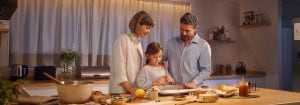 A mother and father stand with their daughter in a well-lit kitchen