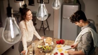 Modern kitchen with vintage style LED pendant lights illuminating two women enjoying dinner, creating warm, inviting atmosphere.